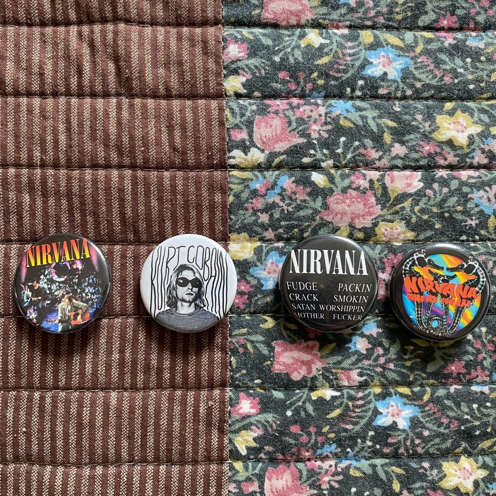Four Nirvana and Kurt Cobain pins of various colors and designs.